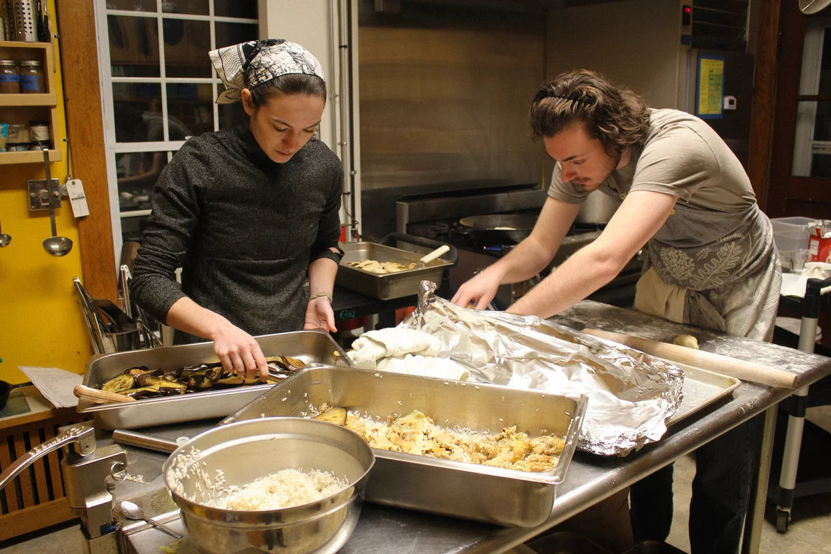 Two roots for refugees team members rolling pita bread in a kitchen.